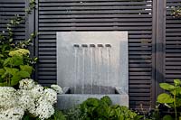 Zinc water fountain and grey fence with Hydrangea Annabelle