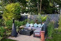 Contemporary London garden with grey painted fence. Wooden post screen - Lower seating area with Chimenea Purple flower is Verbena bonariensis Tree Fern  - Dicksonia Antarctica