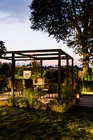 Contemporary London garden in late evening with artificial light looking 
towards pergola and patio eating area