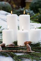 White candles with pine and cones on garden table