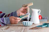 Woman applying the bicarbonate of soda paste to the hand dipper using a wooden spatula. 