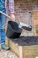 Woman adding soil improver to newly renovated raised bed with a spade. 