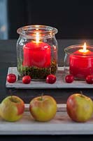 Quick Advent wreath with Malus spec. and apples, 4 red candles in a lantern and moss insde on a table