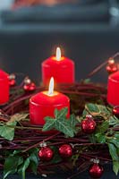 Advent wreath with cornus, ivy, thuya, red Christmas bauble and 4 red candles on a table