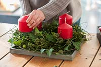Vaccinium myrtillus wreath and ivy cirrus with infructescence  - Advent wreath 
with 4 red candles  - a person making a wreath and placing the candles