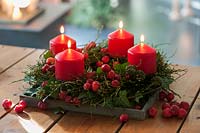 Vaccinium myrtillus wreath and ivy cirrus with infructescence - Advent wreath 
with 4 red candles and Malus spec. berries on the wooden table