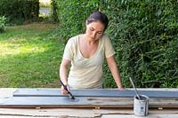 Woman painting the long boards grey using a paint brush