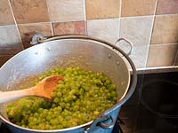 Stirring mixture of green grapes, sugar and lemon juice in metal pan to make jam.  
