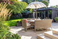Dining furniture with umbrella on modern patio with view to Summerhouse. 