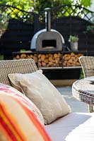View past outdoor cushions on modern garden seating to outdoor pizza oven. 