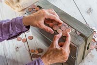 Person gluing coins to wooden box.
