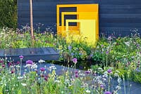 Yellow steel sculptural panels with black fence background in meadow-style planting - 'Urban Oasis', RHS Malvern Spring Festival 2018, sponsored by Graduate Gardeners Ltd. 