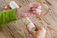 Person winding copper wire around plastic tube to create coiled spring. 