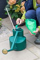Woman adding feed with plastic measuring scoop into watering can. 