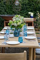 Wooden table and chairs set with plates, glasses and floral arrangements - 'A Garden for all Seasons', Ascot Spring Garden Show, 2018.