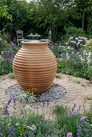 Urn-shaped terracotta water feature sat on pebbles with circular paved and gravel patio - Best of Both Worlds, RHS Hampton Court Palace Flower Show 2018