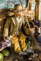 Redundant scarecrow resting in the summerhouse surrounded by gourds and pumpkins and onions drying. RHS Garden Rosemoor, Great Torrington, Devon, UK