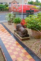 Front garden of Victorian terraced house, featuring a tiled path beside gravelled area containing statuary and planting including Begonia 'Big Boy', Agapanthus and Cordylines. The Secret Garden at Serles House, Dorset, UK. 