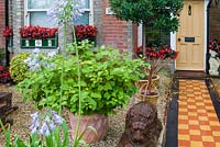 Front garden of Victorian terraced house, featuring a tiled path beside gravelled area containing statuary and potted plants. The Secret Garden at Serles House, Dorset, UK.