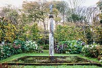 Pleached limes, hydrangeas and square pool with column and statue. Plas Brondanw, Gwynedd, Wales
