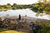 Seating area on boardwalk beside pond with Salix matsudana - Corkscrew willow. Oast House, Isfield, Sussex, UK