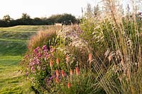 Grasses and Kniphofia with earthwork. The Oast House, Isfield, Sussex, UK