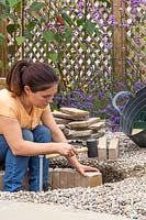 Woman placing bricks in dug hole to create wall of firepit.