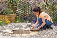 Woman placing pavers at edge of firepit. 