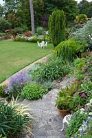 View of mixed planting, terrace and lawn in coastal garden, UK. 