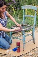 Woman using sandpaper to remove any loose paint from old wooden chair. 