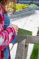 Woman sawing a section of a pallet off with a handsaw. 