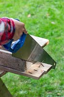 Woman sawing off uneven end of wooden boards with handsaw. 