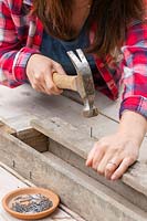 Woman hammering nail into pallet board to create a pallet planter.