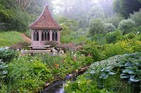 Summerhouse in the bog garden by a stream fringed with moisture loving plants. The Old Rectory, Netherbury, UK.
