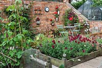 A partly-walled potager of raised beds, planted with climbing beans and 
Antirrhinum majus - snapdragons. The corner of walled area has small seating area with wall used for clematis, pelargoniums and ornaments

