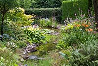 View of a pumped stream, edged in astilbes, daylilies, hostas, ferns and primulas. 