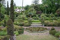 Overview of a garden with formal waterlily pond and a series of terraced beds leading up to woodland and house