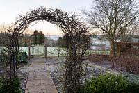 Arch of Japanese quince frames a path between frosted beds in the kitchen garden and to a gate into adjoining field