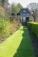A grassy path between a box hedge and a mixed border leads towards the Orangery at Plas Brondanw, Penrhyndeudraeth, Gwynedd, Wales