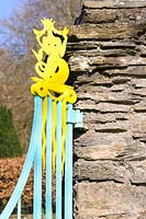 Decorative metalwork around the garden is painted in bright yellow and turquoise, here a mermaid on a gate in the boundary wall. Plas Brondanw, Penrhyndeudraeth, Gwynedd, Wales