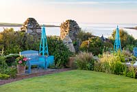 View of blue painted bench and obelisks in seaside garden. 