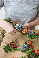 Person using floristry wire to attach a fir cone to a decorated Christmas wreath. Step-by-Step for making a Christmas Tree shaped door wreath.