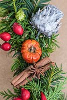 Detail of decoration of Christmas door wreath, with cinnamon sticks, dried mini pumpkins, star anise, hops, rose hips and a silver cardoon flower.