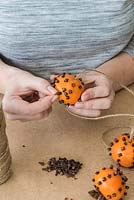Woman studding clementines with cloves to make scented pomander decorations.
