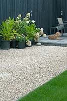 View of gravel garden with potted plants and dog on terraced patio. 