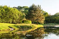 Lake surrounded by trees and lawn, Plaz Metaxu Garden, Devon, UK. 