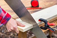 Sawing through piece of wood held with table clamps.