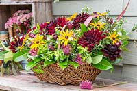 View of finished floral arrangement in wicker basket, with Rudbeckia, Dahlia,
 Sedum and Phormium leaves
