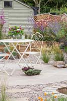 Ornate metal table and chairs on circular patio in gravel garden