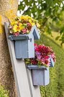 Pair of wooden birdboxes with flower embellished roofs mounted on painted planks